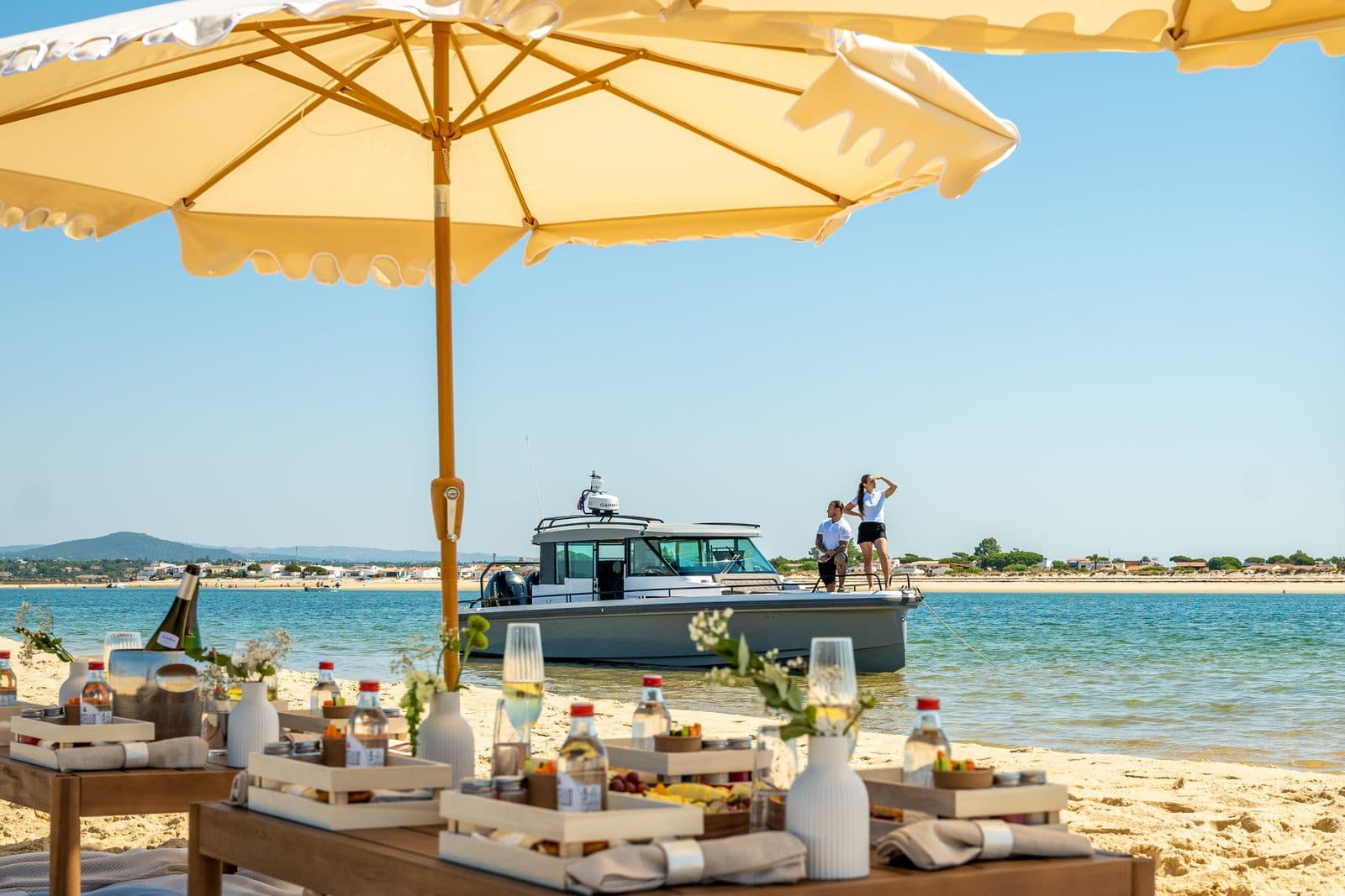 Arkeo moored behind a parasol and a set lunch table on the sandbank