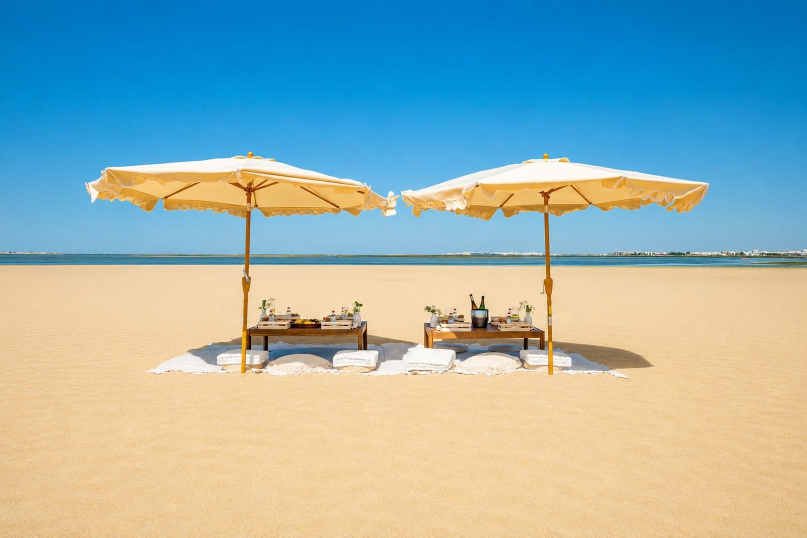 Two parasols and low tables set for lunch on an empty sandbank